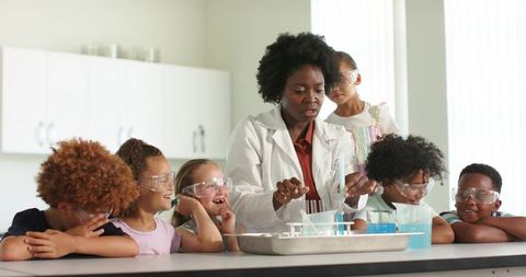 Teacher demonstrating hands-on chemistry experiment with curious students wearing safety goggles