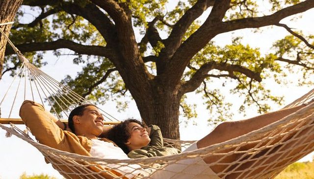 Young couple relaxing in hammock under oak tree on sunny afternoon enjoying leisure time in nature