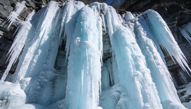 Massive frozen waterfall cascading into towering blue ice pillars on rugged cliff face