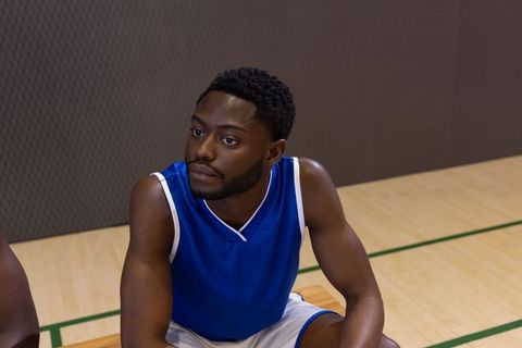 African american basketball player sitting on bench wearing blue jersey contemplating game