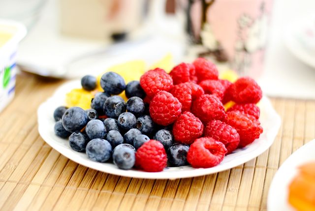 Fresh blueberries and raspberries on a white plate creating a vibrant and colorful display. Great for use in articles, blogs, and websites promoting healthy eating, organic food, and recipes. Ideal for illustrating breakfast options, nutrition content, and healthy lifestyle topics.