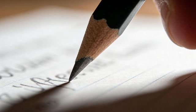 Macro closeup pencil writing on lined paper with fingertip gripping sharpened graphite tip