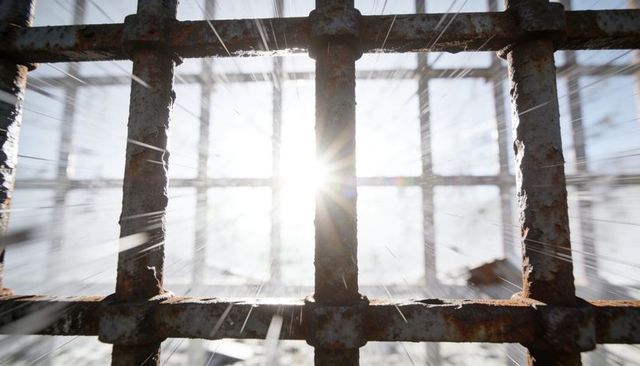 Rusted metal grid backlit by bright sun flare with cobwebs on weathered industrial bars