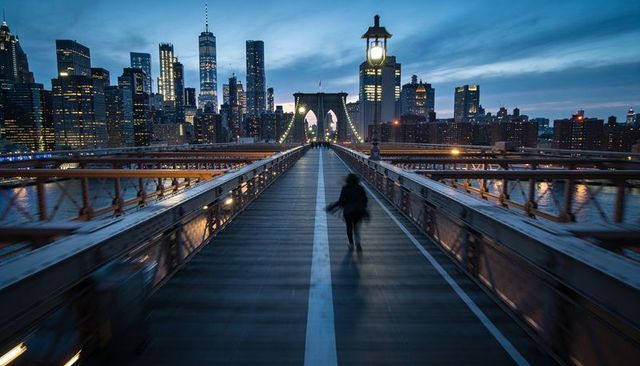 Walking on brooklyn bridge at dusk with manhattan skyline, lit arch and lone pedestrian