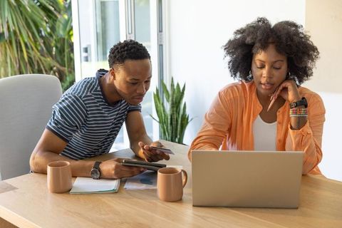 African american couple working together at home desk using laptop tablet and smartphone