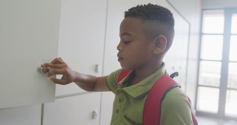 an african american boy with a backpack is closing a locker and smiling in a school setting. this image represents themes of education, student life, and daily school activities. ideal for use in educational materials, school websites, or advertising related to childhood education and learning environments.
