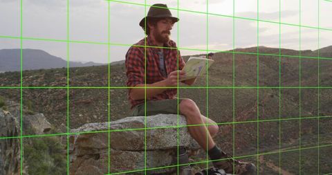 Explorer Studying Map on Rock Ledge in Rugged Terrain