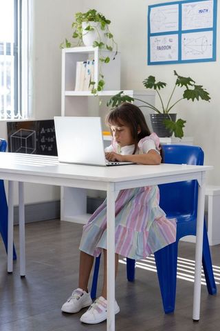Young girl studying on laptop in bright sunlit classroom, focusing on online learning