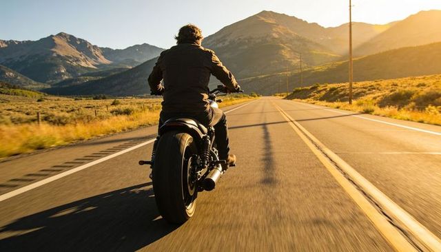 Motorcyclist riding through mountain valley at golden hour on open rural highway