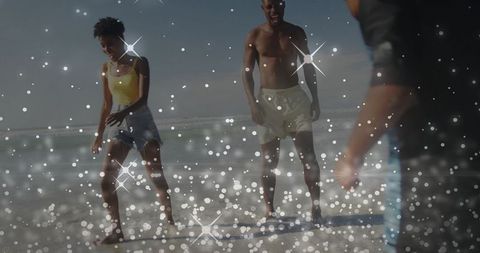 Laughing family walking in shallow surf on sunny beach with sparkling bokeh lights