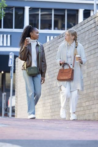 Black and white friends walking and chatting with takeaway coffee on urban brick walkway