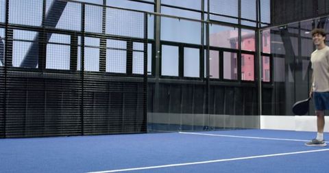 Male athlete holding padel racket on blue court near urban building