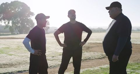 Coaches discussing training on sunlit sports field with three men in dark athletic wear