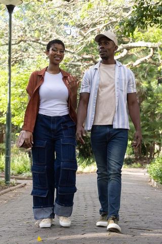African american couple walking and talking under tree canopy in urban park