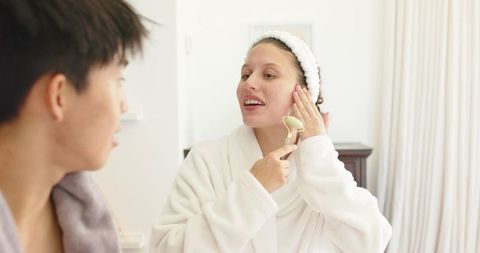 Diverse couple sharing morning skincare routine with green jade roller and bathrobes