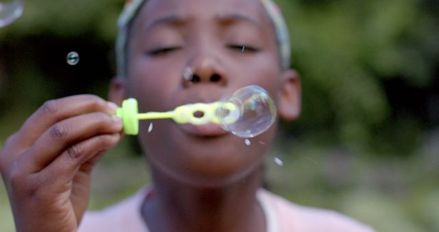 Portrait of happy african american girl blowing bubbles in garden. Lifestyle, childhood, spring, happiness, unaltered.