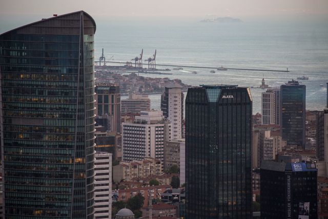 High-rise buildings overlooking ocean with distant boats and cranes along the waterfront. Use this image for cityscape themes, urban development, and modern architecture concepts.