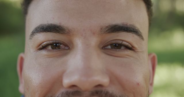 Close-up view of a young man's face with a joyful smile against a nature background. Ideal for use in advertisements, blogs, websites, and other media focusing on youth, happiness, positive emotions, lifestyle, and outdoor activities.