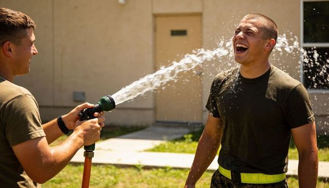 Soldiers playfully spraying water with hose during training break laughing and cooling off