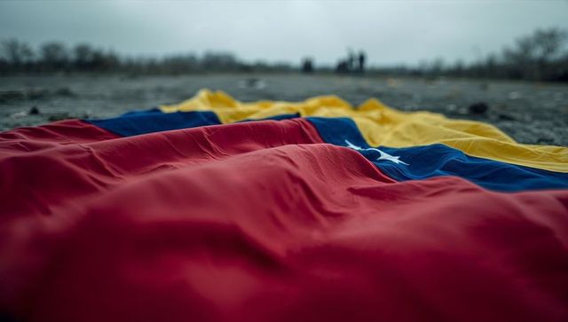 Venezuelan flag lying on pebble shore with distant silhouettes under moody sky