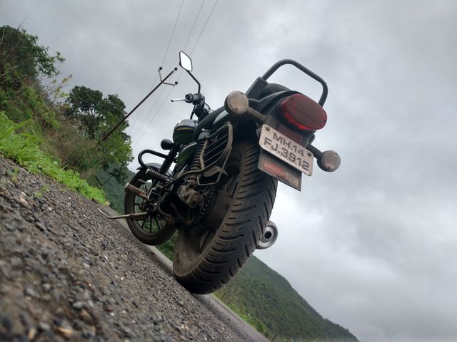 Low angle view highlighting a vintage motorcycle parked on a rural road with cloudy sky backdrop. Ideal for use in travel and adventure-themed projects, promoting biker lifestyle, showcasing the beauty of countryside travel, or emphasizing freedom and road trips.