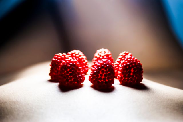 Bright red raspberries resting on a smooth surface, set against a contrasting background, capturing their texture and juicy appeal. Suitable for use in healthy eating campaigns, fruit and recipes blogs, summer-themed promotions, and food-related editorials.