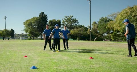 Diverse male athletes practicing team training drill with cones on sunny outdoor sports field