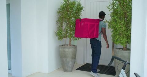 African american courier delivering bright pink backpack to modern residential entrance