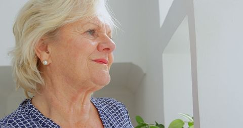 Senior woman reflecting by window in bright home interior