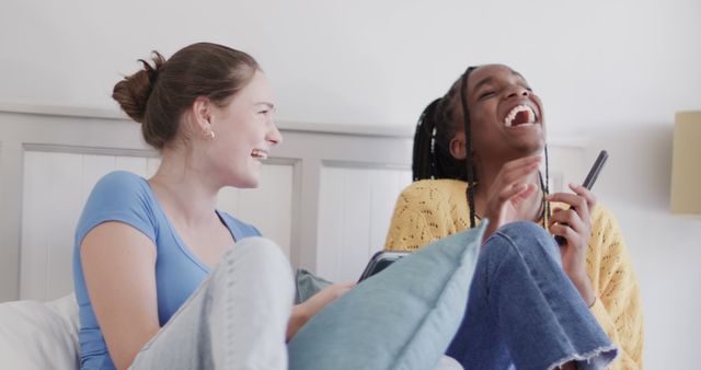 Two Relaxed Young Women Laughing on Bed with Smartphones at Home - Download Free Stock Images Pikwizard.com