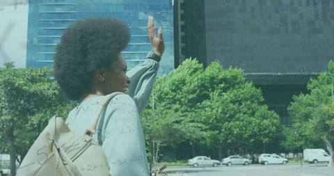 Woman walking in city with backpack, raising hand in urban setting