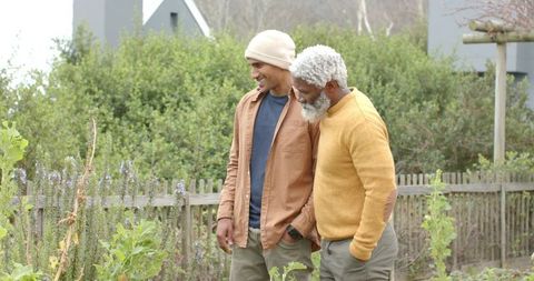 Diverse male friends walking through neighborhood garden inspecting tall flowering plants