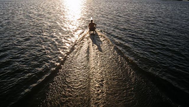 Solo kayaker paddling into golden sunset casting long wake and dramatic reflection on lake