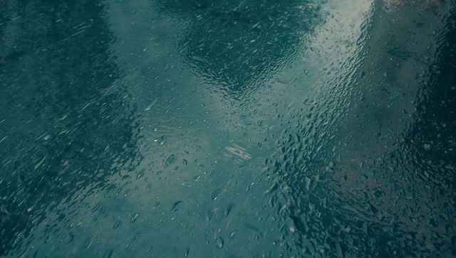 Moody wet glass reflecting urban skyline with raindrops