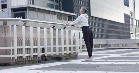 Mature Woman Stretching on Urban Bridge in Hoodie and Sneakers for Morning Wellness
