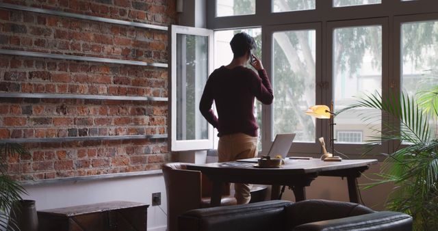 Man Talking on Phone in Stylish Home Office with Large Windows and Brick Walls - Download Free Stock Images Pikwizard.com