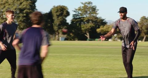 Diverse male teammates practicing catch drill on field during fitness training