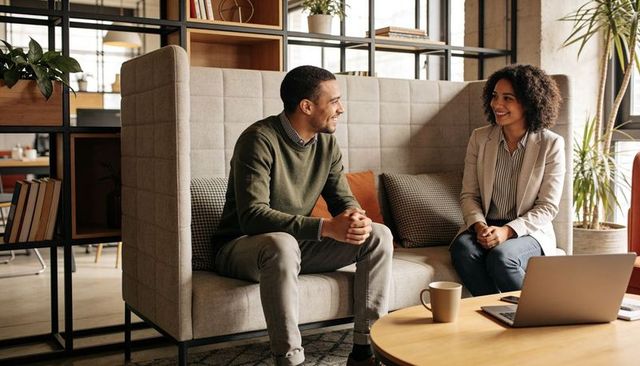 Colleagues collaborating and chatting on banquette in modern office lounge with laptop