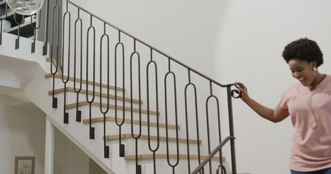 Woman Joyfully Descending Modern Staircase, Smiling Sunlit Interior
