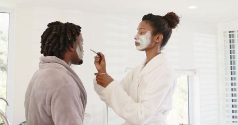 African american couple putting on face masks together in bright modern bathroom