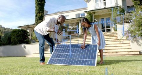 Parent and child installing solar panel on suburban lawn teaching renewable energy