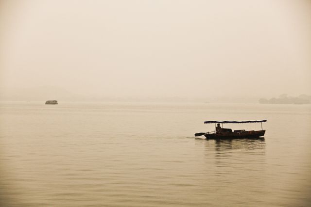 Calm, tranquil scene of a single boat floating on a misty lake at dawn, perfect for themes of solitude, peace, and serenity. Suitable for travel brochures, meditation backgrounds, desktop wallpapers, and nature blogs.