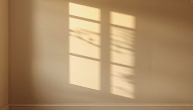 Sunlit window grid casting soft blind and foliage shadows on beige wall