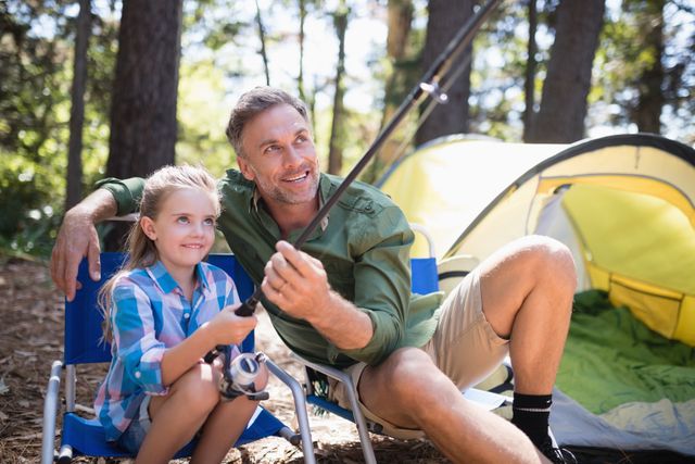 Happy father and daughter fishing at campsite in forest
