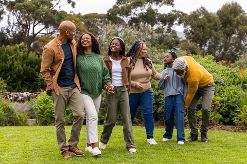 Multigenerational african american family strolling in park, holding hands and laughing