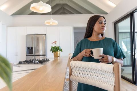 African american woman enjoying morning coffee in modern sunlit open-plan kitchen