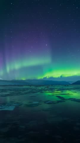 Aurora borealis dancing over frozen lake with starry sky reflection vertical video