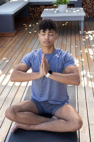 African man practicing outdoor meditation on wooden deck sitting calmly with smartwatch