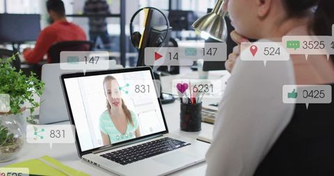 Office worker on laptop watching video call and tracking social engagement in open office