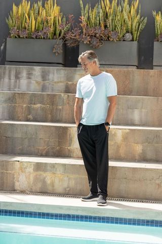 Relaxed senior man standing at pool edge wearing wristwatch in minimalist courtyard